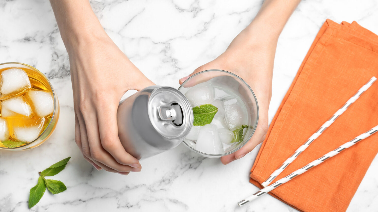 Woman pouring drink from tin can into glass at table, top view