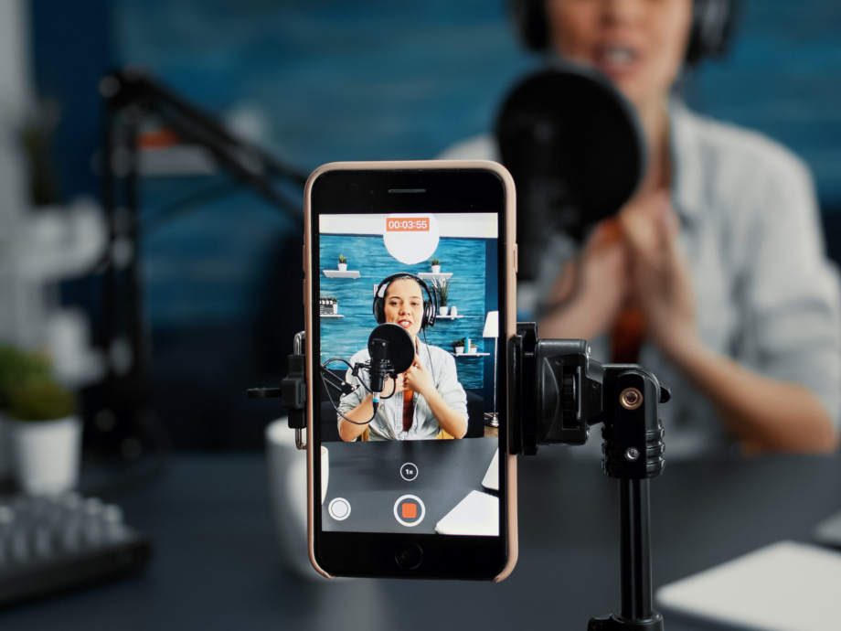 Modern smartphone recording vlogger talking to public while sitting at home studio desk. Famous influencer filming podcast show with touchscreen display device while sitting in living room. Close up